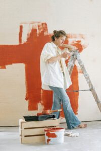 woman in white shirt and blue denim jeans standing beside red wall